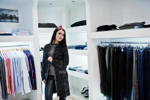 Brünettes wunderschönes Mädchen in der Boutique des Bekleidungsgeschäfts in Freizeitkleidung und grauem Mantel. foto
