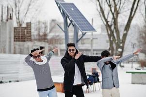 Gruppe von drei lässigen jungen indischen Männern mit Sonnenbrillen, die am Wintertag gestellt wurden, zeigt Dab. foto