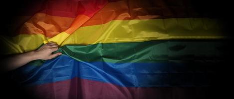 lgbtq-stolzflagge auf schwarzem hintergrund. lgbt-regenbogenfahne in schwuler hand. foto