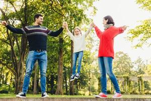 Aufgeregtes kleines Kind, das froh ist, Zeit mit seinen Eltern zu haben, Steine in der Hand, lächelt glücklich. Verspieltes, entzückendes Mädchen mit fröhlichem Ausdruck, verbringt gerne Zeit mit Vater und Mutter. foto