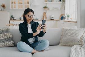 junge hispanische frau hat einen videoanruf, entspannt sich und surft mit dem handy durch das internet. foto