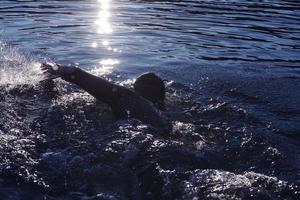 Triathlon-Athlet, der bei Sonnenaufgang auf dem See schwimmt und einen Neoprenanzug trägt foto