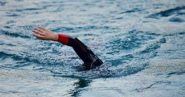 Triathlon-Athlet, der bei Sonnenaufgang auf dem See schwimmt und einen Neoprenanzug trägt foto