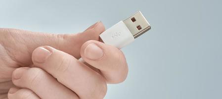 Hand, die weißes USB-Kabel auf grauem Hintergrund isoliert hält. foto