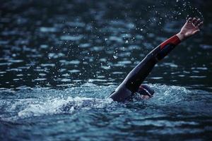 Triathlon-Athlet, der bei Sonnenaufgang auf dem See schwimmt und einen Neoprenanzug trägt foto