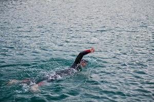 Triathlon-Athlet, der bei Sonnenaufgang auf dem See schwimmt und einen Neoprenanzug trägt foto