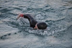 Triathlon-Athlet, der bei Sonnenaufgang auf dem See schwimmt und einen Neoprenanzug trägt foto