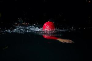 Triathlon-Athlet schwimmt in dunkler Nacht und trägt einen Neoprenanzug foto