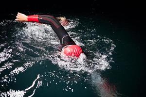 Triathlon-Athlet schwimmt in dunkler Nacht und trägt einen Neoprenanzug foto