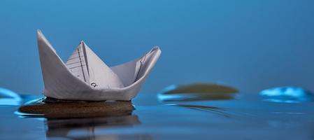 Papier-Origami-Boot auf dem Stein im blauen Wasser. Foto mit Kopierbereich.