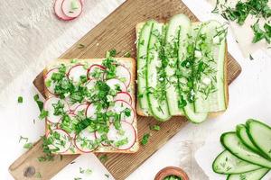 Sandwiches mit Weichkäse Rettich und Gurke auf einem Holzbrett. gesundes Frühstück. foto