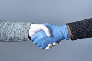 das Konzept eines sicheren Händedrucks. Händeschütteln in medizinischen Handschuhen auf grauem Hintergrund foto