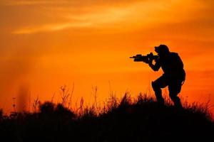 Silhouette des Militärsoldaten oder des Offiziers mit den Waffen bei Sonnenuntergang