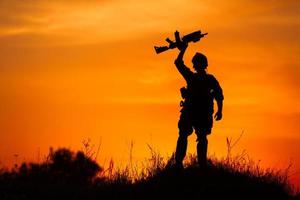 Silhouette des Militärsoldaten oder des Offiziers mit den Waffen bei Sonnenuntergang