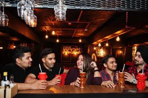 gruppe indischer freunde, die sich im nachtclub amüsieren und ausruhen, cocktails in der nähe der bartheke trinken. foto