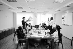 Ein gemischtrassiges Geschäftsteam trifft sich am Sitzungstisch, zwei Teamleiter werfen Papier hoch. foto