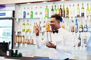 Afroamerikanischer Barkeeper an der Bar mit Shaker. Zubereitung von alkoholischen Getränken. foto