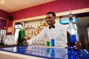 Afroamerikanischer Barkeeper an der Bar, der Cocktails auf Aufnahmen macht. Zubereitung von alkoholischen Getränken. foto