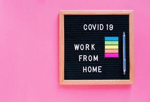 Flache Lage der Anschlagtafel mit Slogan-Nachricht Arbeit von zu Hause aus und Kovid-19 auf rosa Hintergrund mit Kopierraum, Selbstquarantänekonzept, Kovid-19 und Coronavirus verhindern foto