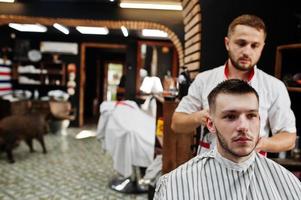 junger bärtiger mann, der vom friseur die haare schneiden lässt, während er im friseursalon auf dem stuhl sitzt. Barbier Seele. foto