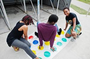 Gruppe von drei afroamerikanischen Freunden spielen Twister-Spiel im Freien. foto