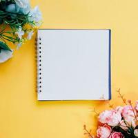 flache lage des minimalen arbeitsbereichs leeres notizbuch mit blume auf gelbem hintergrund, frühlings- und sommerkonzept foto
