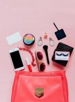 flache lage aus rosa lederfrauentasche offen mit kosmetik, accessoires, tag-karte und smartphone auf rosa hintergrund mit kopierraum foto