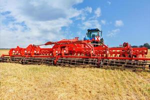 Universelle rote Egge als Anhängerkupplung an einem landwirtschaftlichen Traktor vor dem Hintergrund eines komprimierten gelben Weizenfeldes. foto