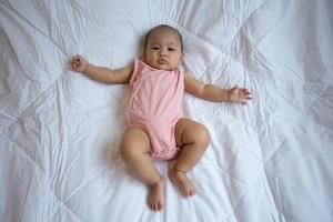 asiatisches süßes baby im weißen sonnigen schlafzimmer. neugeborenes kind entspannt sich im bett foto