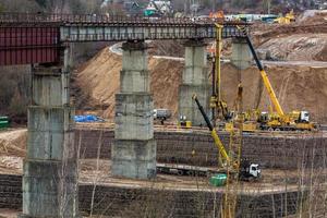 Bau oder Wiederaufbau einer Autobahnbrücke aus Beton über einen breiten Fluss. Baumaschinen, Lastwagen und Kräne arbeiten foto