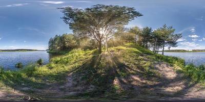 Vollständiges, nahtloses sphärisches HDRI-Panorama 360-Grad-Winkelansicht in der Nähe eines riesigen Baums am Ufer eines breiten Flusses mit Sonnenstrahlen durch Äste in äquirechteckiger Projektion, bereit für virtuelle Realitätsinhalte foto