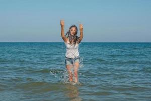 junges Mädchen, das das Wasser im Meer spritzt foto