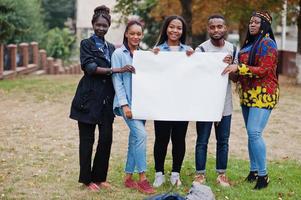 eine gruppe von fünf afrikanischen college-studenten auf dem campus des universitätshofs hält einen leeren weißen rohling. Freiraum für Ihren Text. Schwarze Afro-Freunde studieren. foto