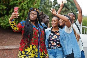 Gruppe von fünf afrikanischen College-Studenten, die gemeinsam Zeit auf dem Campus des Universitätshofs verbringen. schwarze afro-freunde, die selfie am telefon machen. Thema Bildung. foto