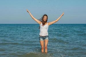 junges Mädchen, das das Wasser im Meer spritzt foto