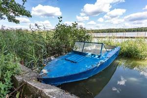 Altes blaues Holzboot am Ufer eines breiten Flusses an sonnigen Tagen foto