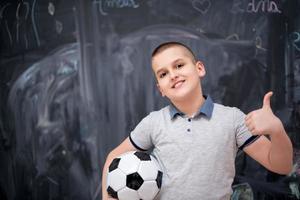 glücklicher junge, der einen fußball vor tafel hält foto