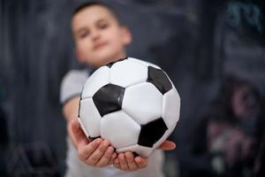 glücklicher junge, der einen fußball vor tafel hält foto