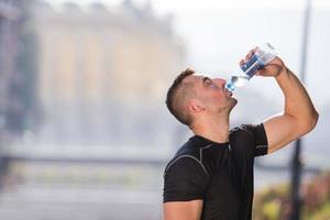 Mann, der nach dem Joggen Wasser aus einer Flasche trinkt foto