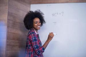 Afroamerikanerin schreibt auf einer Tafel in einem modernen Büro foto