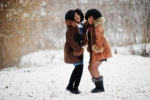 zwei lockige haare afroamerikanerinnen tragen einen schaffellmantel und handschuhe, die am wintertag gestellt wurden. foto