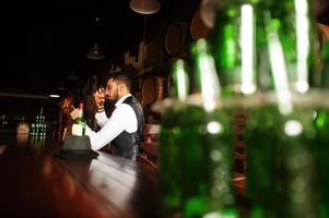 hübscher, gut gekleideter arabischer mann mit einem glas whisky und einer zigarre, die im pub posiert. foto