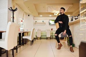 arabischer mann trägt schwarze jeansjacke und brille im café trinken kaffee an der bar mit buch. stilvoller und modischer arabischer Modelltyp. foto