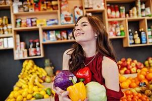 Mädchen im Rot, das verschiedenes Gemüse auf Obstspeicher hält. foto