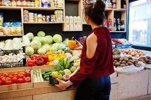 Mädchen im Rot, das verschiedenes Gemüse auf Obstspeicher hält. foto