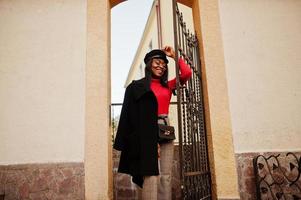 afroamerikanisches modemädchen in mantel und zeitungsjungenmütze posierte auf der straße. foto