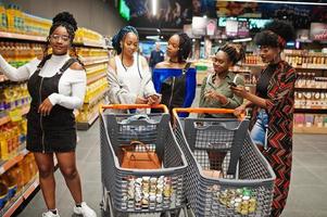 Gruppe von fünf afrikanischen Frauen, die mit Einkaufswagen im Supermarkt spazieren gehen. foto