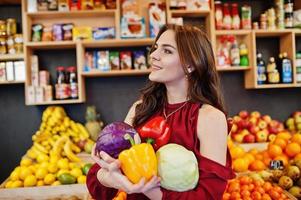 Mädchen im Rot, das verschiedenes Gemüse auf Obstspeicher hält. foto