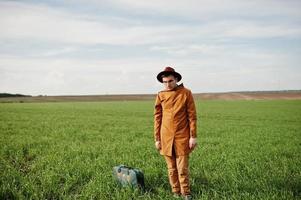 Stilvoller Mann mit Brille, brauner Jacke und Hut mit Tasche auf der grünen Wiese. foto