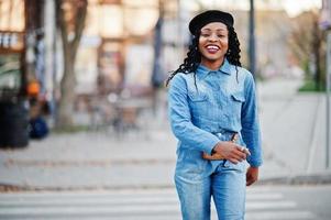 stilvolle modische afroamerikanische frauen in jeans und schwarzer mütze, die auf dem fußgängerverkehr laufen.